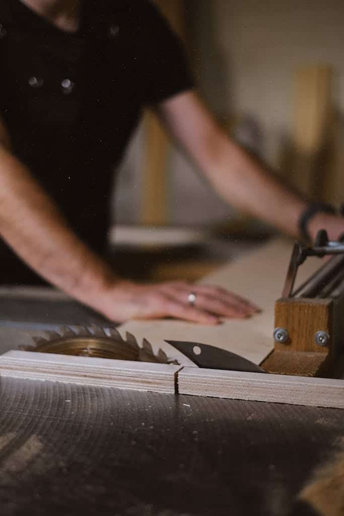 Unrecognizable blurred male master cutting wooden plank using table saw with sharp knives while working in professional workshop with special instruments