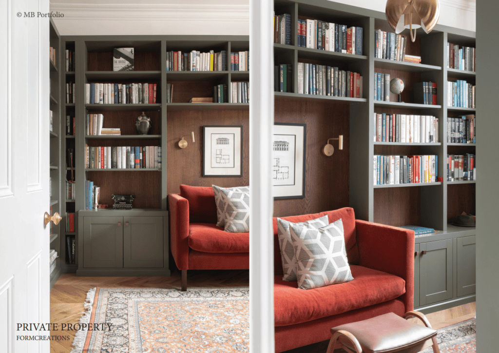 Elegant home library with dark wood bookshelves filled with books, framed by a green wall with two identical cozy red sofas and decorative pillows. middle column partially obstructs view.