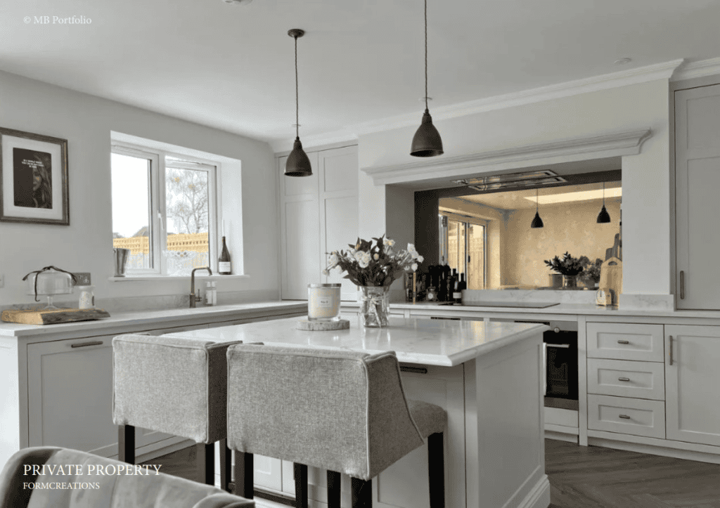 A modern kitchen with white cabinetry, a central island with bar stools, pendant lights, and a view into an adjacent room. neutral tones and natural light create an elegant atmosphere.