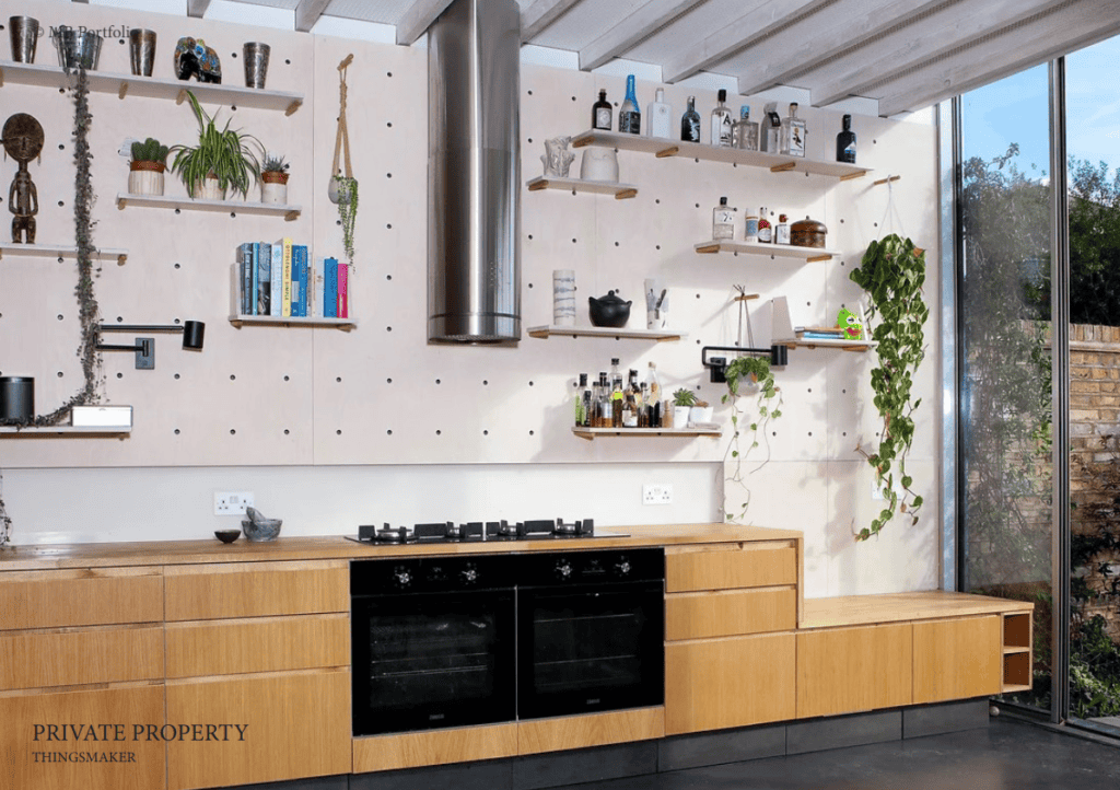 A modern kitchen with wooden cabinets, a central cooking island, and wall-mounted shelves filled with plants and bottles. large windows let in natural light.